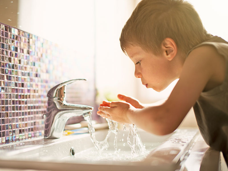 Little boy aged 4 is drinking tap water in sunlit bathroom